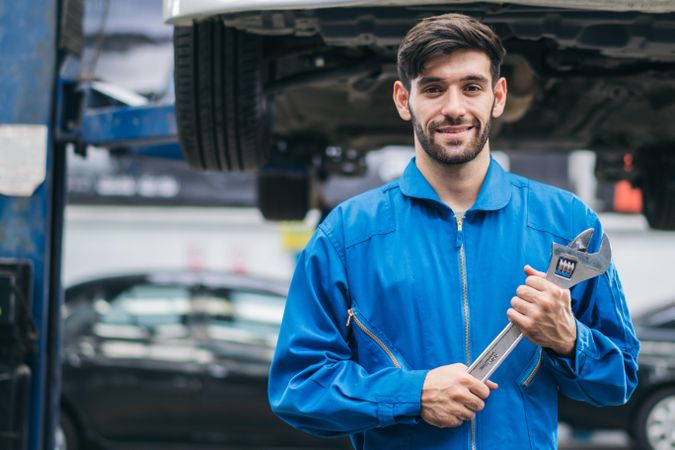 Happy white male mechanic holding wrench at auto garage