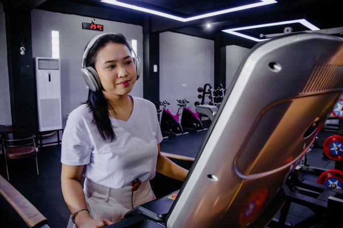 Young woman enjoying music on a treadmill in a well-lit gym
