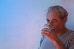 Portrait of middle aged man in gray shirt drinking water against light background in UV lit studio