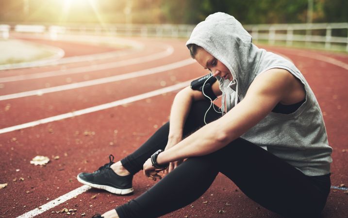 Woman in hooded vest sitting on running track