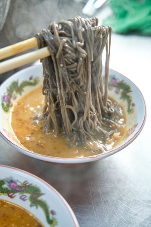 Traditional Japanese noodles on chopsticks in bowl with broth