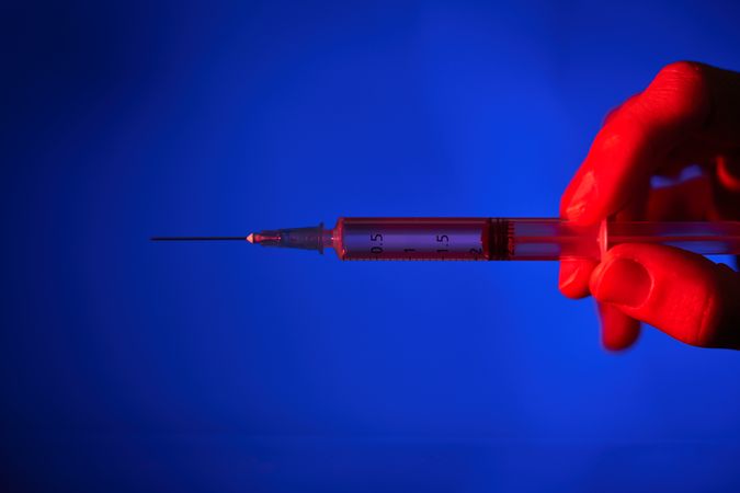 Anonymous person with syringe in neon lighting
