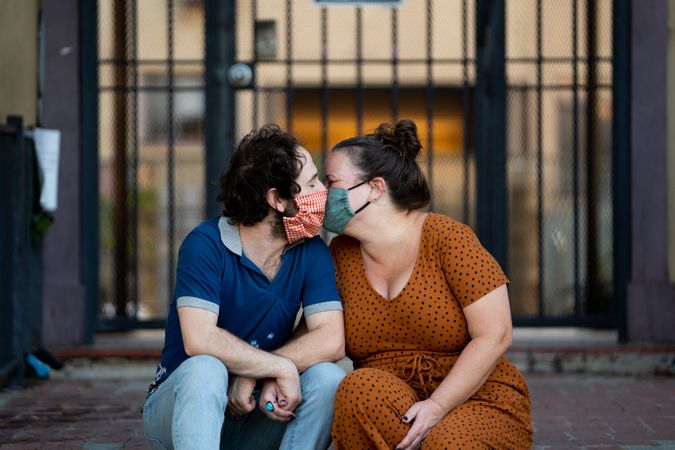 Romantic couple sitting outside in the evening kissing with masks on