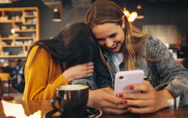 Cheerful young women using smart phone with a cup of coffee on the table