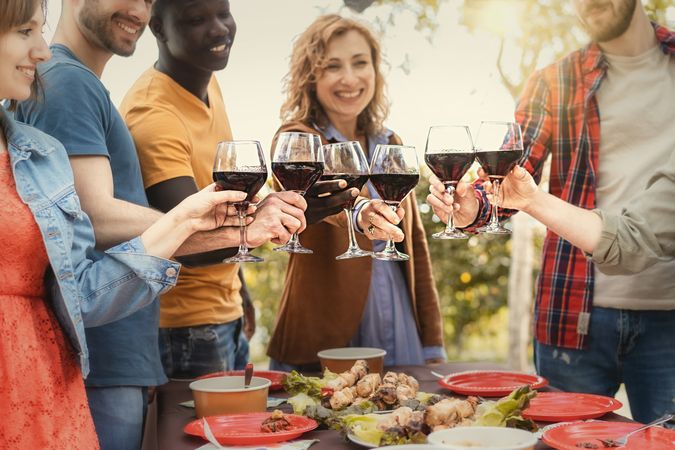 Toasting with red wine glasses over a meal on an outdoor table