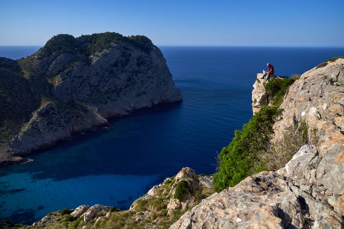 Unrecognizable traveler on rocky cliff near sea