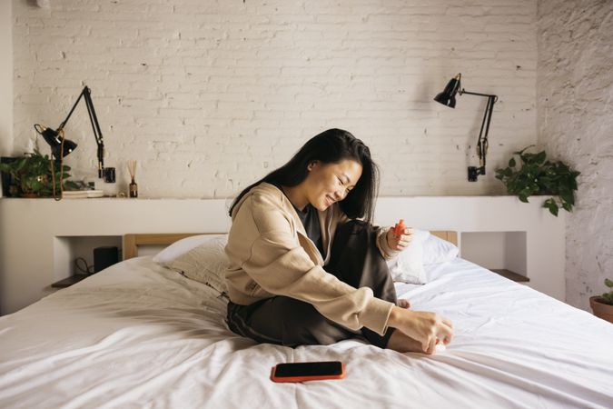 Young woman doing pedicure on bed