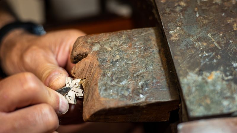 Goldsmith working and creating in his crafting gold jewelry workshop with a burin. Jeweler repairing a silver jewel.