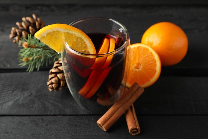 Glass of tasty mulled with orange on decorated background, space for text
