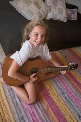 Positive kid sitting on floor and playing guitar