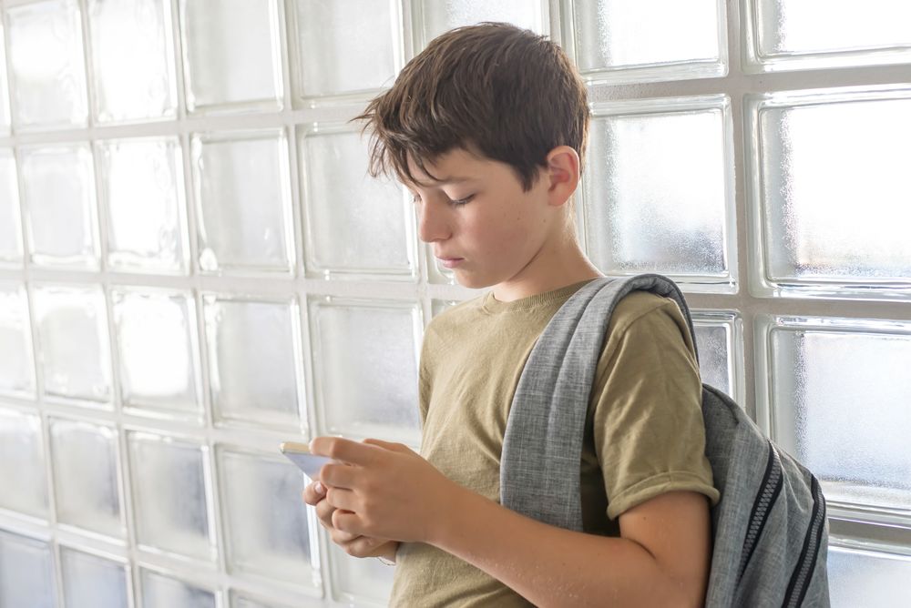 Sad teenager texting while leaning on wall
