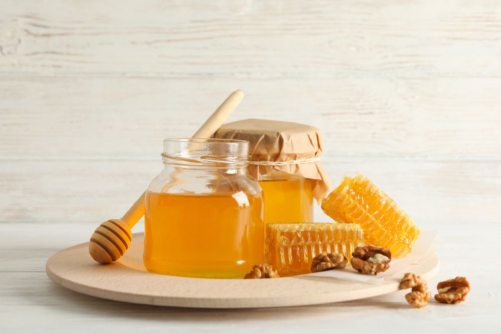 Honeycombs, walnuts, dipper and jars with honey on wooden background, copy space