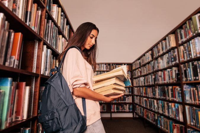 Young woman holding textbooks while reading book in library