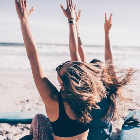 Two young women raising their hands in the air at the beach