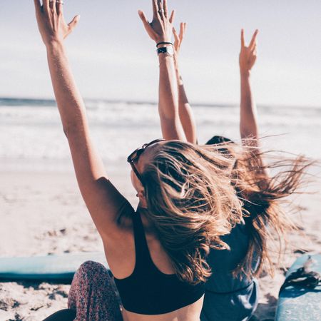 Two young women raising their hands in the air at the beach
