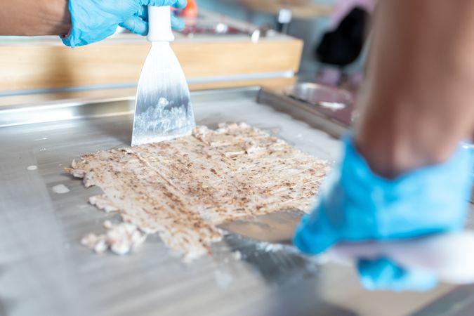 A worker is using spatulas to flatten a chocolate mix on a rolled ice cream machine