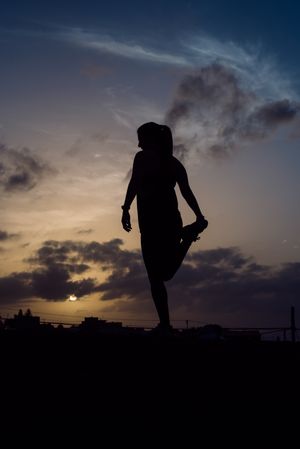 Stretching woman and sky with clouds at sunset