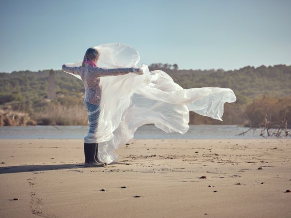 Girl caught up in plastic sheet standing on sandy shore