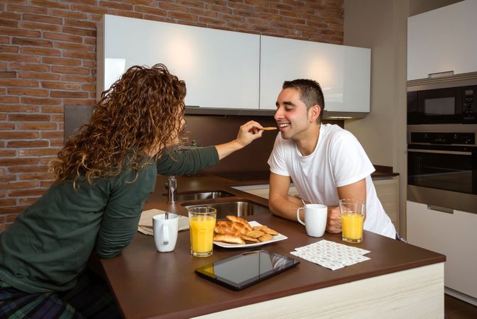 Woman affectionately feeding man breakfast of pastries