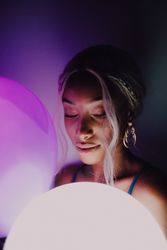 Black adult woman with illuminated balloon in darkness looking at camera