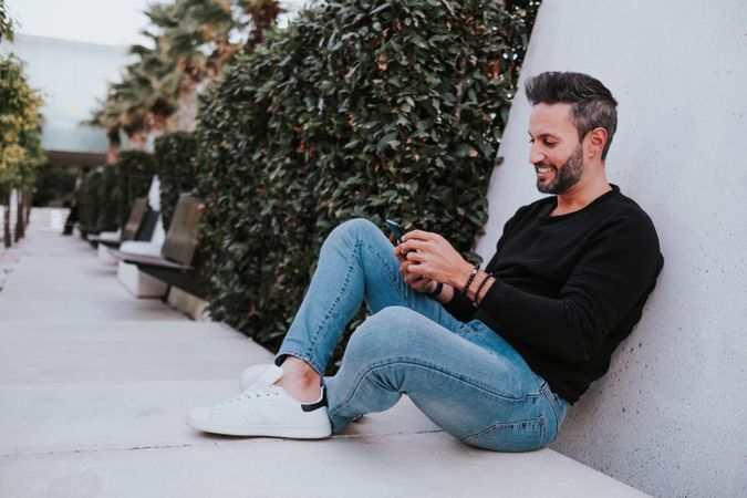Adult stylish smiling man using a smartphone near grey wall