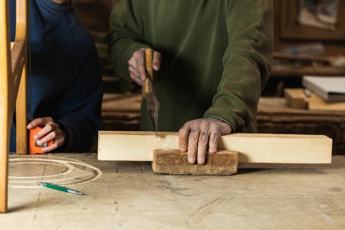 Joiner cutting wood with colleague measuring height