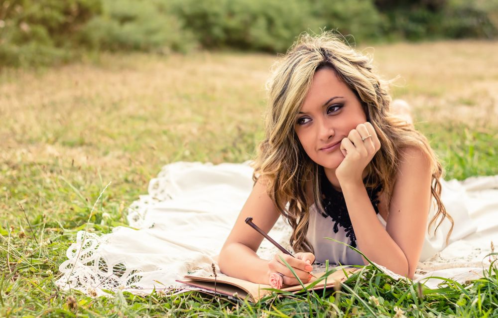 Romantic woman writing in a diary lying down outdoors