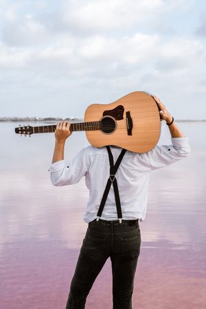 Musician gazing and carrying guitar behind back while standing on beach