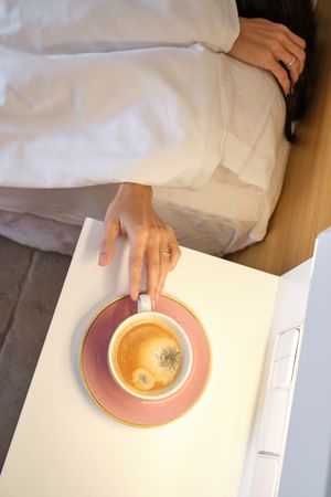Unrecognizable female reaching out coffee mug at bedside