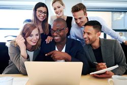 Laughing business associates huddled around a laptop in an office