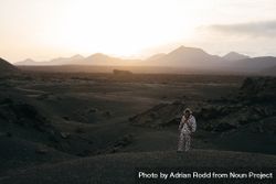 Person in brightly patterned clothes and mask standing on volcanic hills in Lanzarote at dusk 5RWpA4