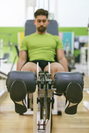 Male in green t-shirt working out quads using gym equipment