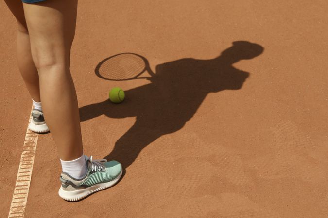 Woman in sneakers on clay court with tennis ball