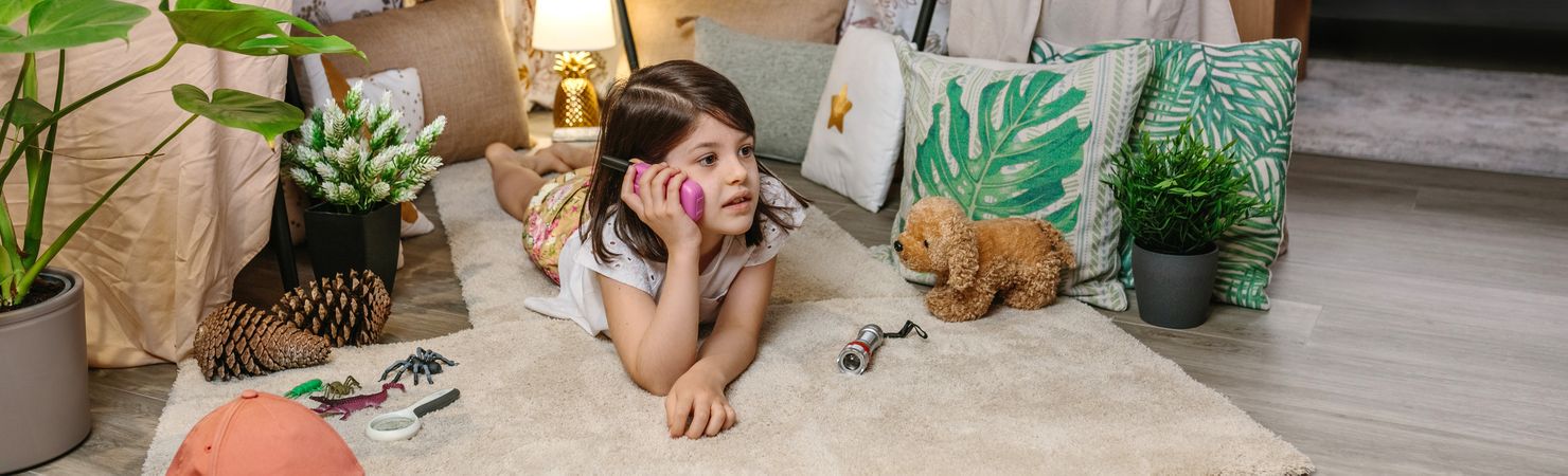 Banner of little girl talking with walkie-talkie lying over rug in tent surrounded by cushions