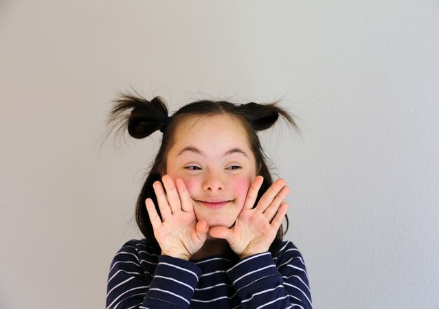 Playful child looking to the side with hands near her face