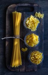 Top view of different pasta shaped on wooden board