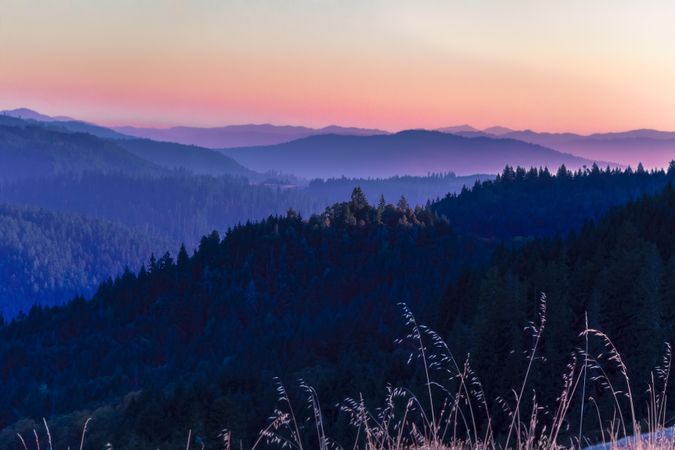 View of vast tree lined mountains under a colorful sky