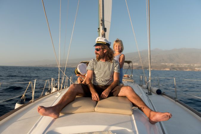Man with smiling children and sitting on deck of yacht in sea