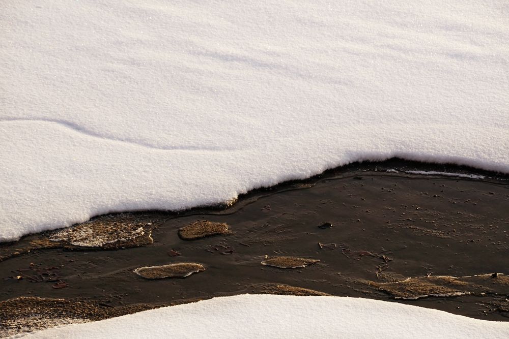 River covered with ice and snow with thawing crack