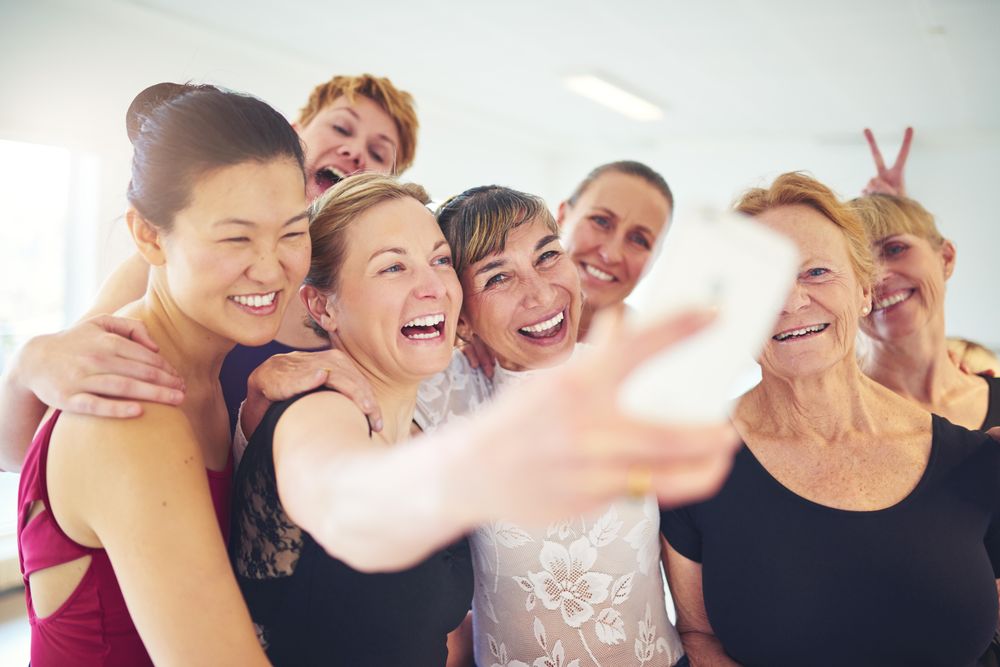 Group of laughing women pose for selfie in bright dance studio