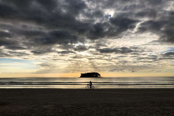 Silhouette of person riding bicycle near ocean during sunset