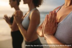 Three women in fitness wear doing yoga and meditation standing at the seashore 4dQ7ab