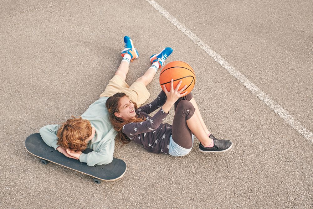 Content teen friends lying on street with skateboard and basketb