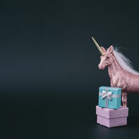 Pink glitter unicorn with wrapped presents on dark background