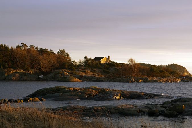 Rocky shore with house of tranquil sea in dusk