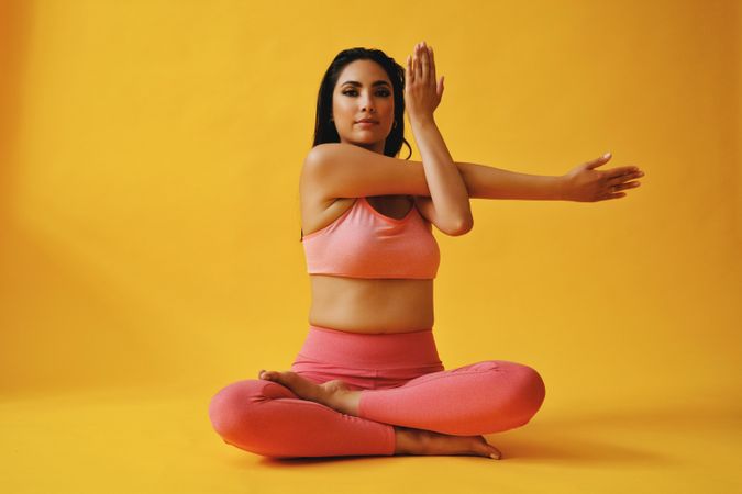 Hispanic female sitting in meditative yoga pose stretching her arm yellow studio shoot