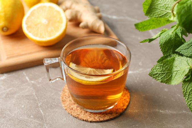Cup of tea, lemon, ginger and mint on grey background, close up