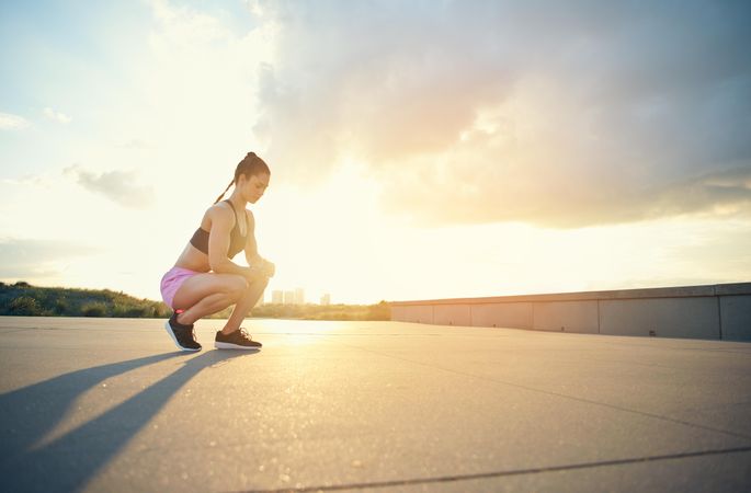 Woman crouching down with bright sunrise and cityscape in background