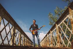 Man with guitar standing on bridge