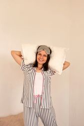 Woman smiling, holding pillows while standing in bed.